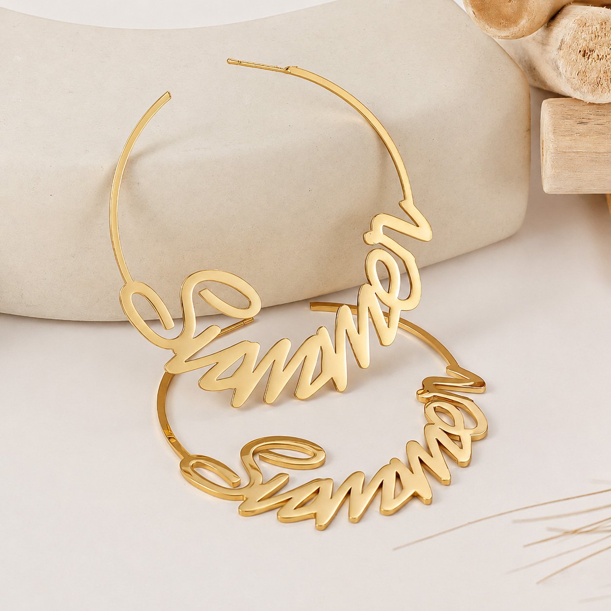 Gold Custom Name Hoop Earrings with a personalized cursive name design displayed on a neutral stone backdrop