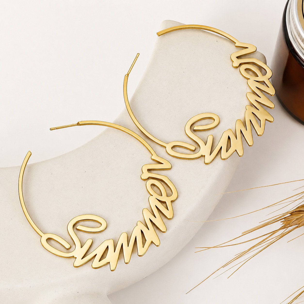 Gold Custom Name Hoop Earrings with a personalized cursive name design displayed on a neutral stone surface