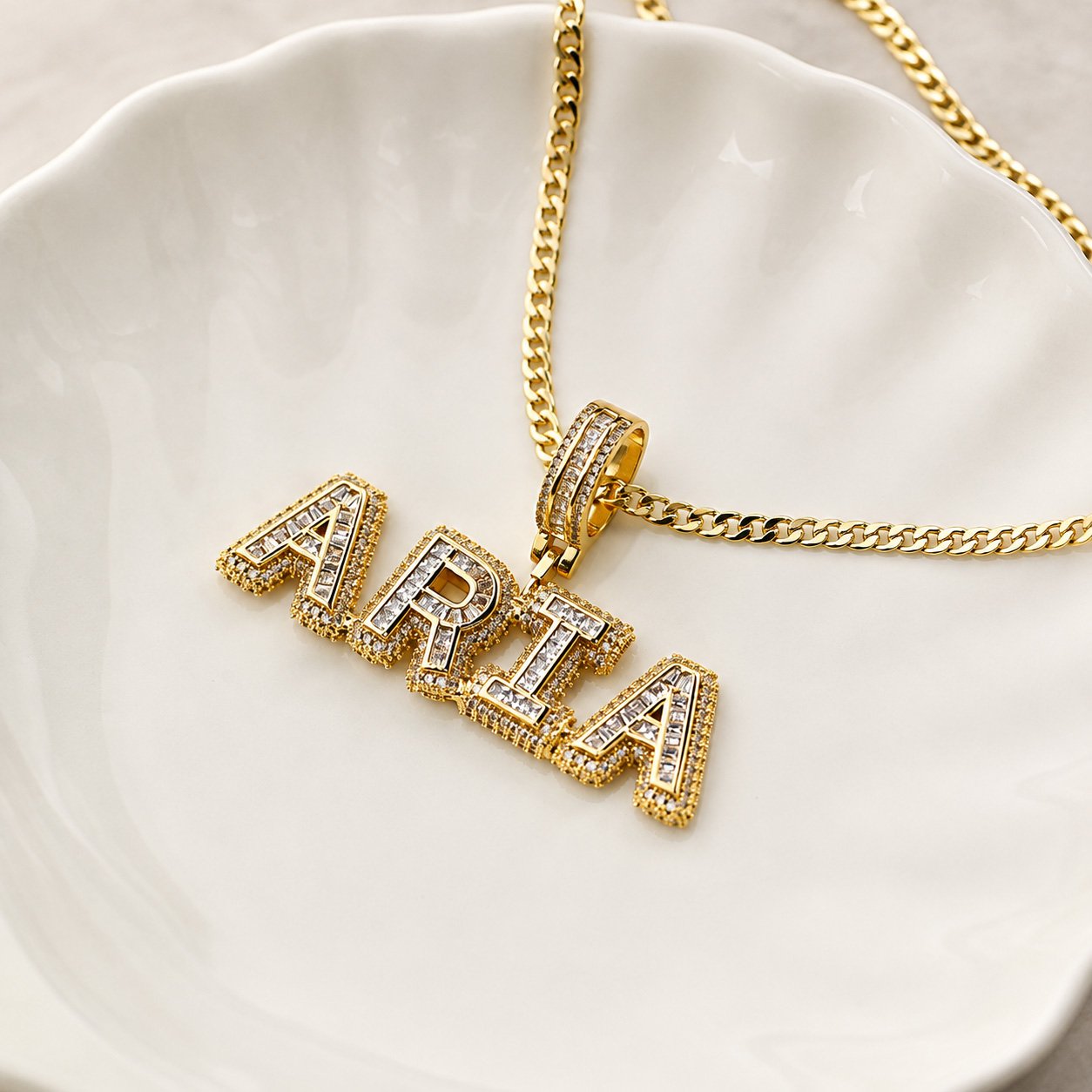 Gold Unisex Premium Bling Name Necklace personalized with “ARIA” displayed on a white ceramic dish