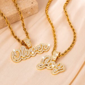 Two gold Crystal Cursive Name Necklaces with sparkling custom name pendants, crystal-studded bails, and rope chains displayed on cream satin